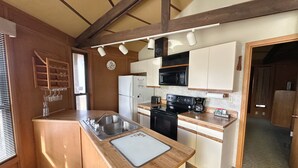A compact kitchen with a sink, stove, microwave, and white cabinets. - Eagle’s Landing Cabin - Eagle River, WI - 3 Bedrooms - 2 Bathrooms (Eagle River)