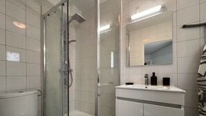 A modern bathroom with a toilet, a glass-enclosed shower, and a vanity with a mirror. - Refined Apartment With Courtyard in La Mans (Le Mans)