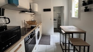A compact kitchen with a coffee maker, washing machine, and a dining area with a table and bench. - Refined Apartment With Courtyard in La Mans (Le Mans)