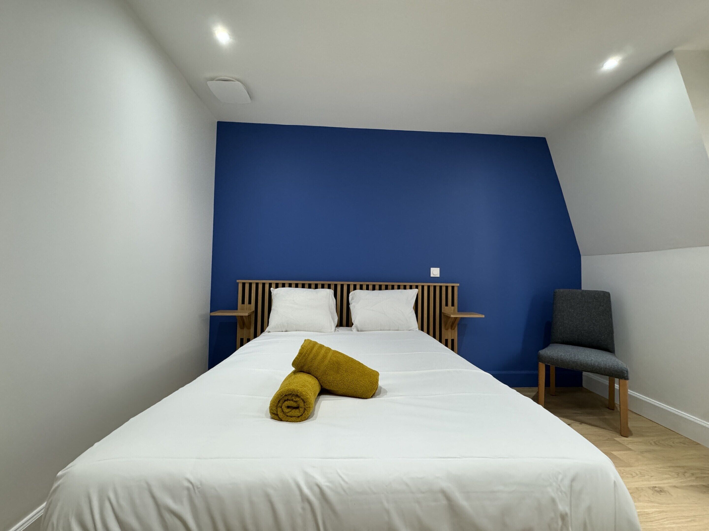 A bedroom with a bed, a chair, and a blue accent wall.