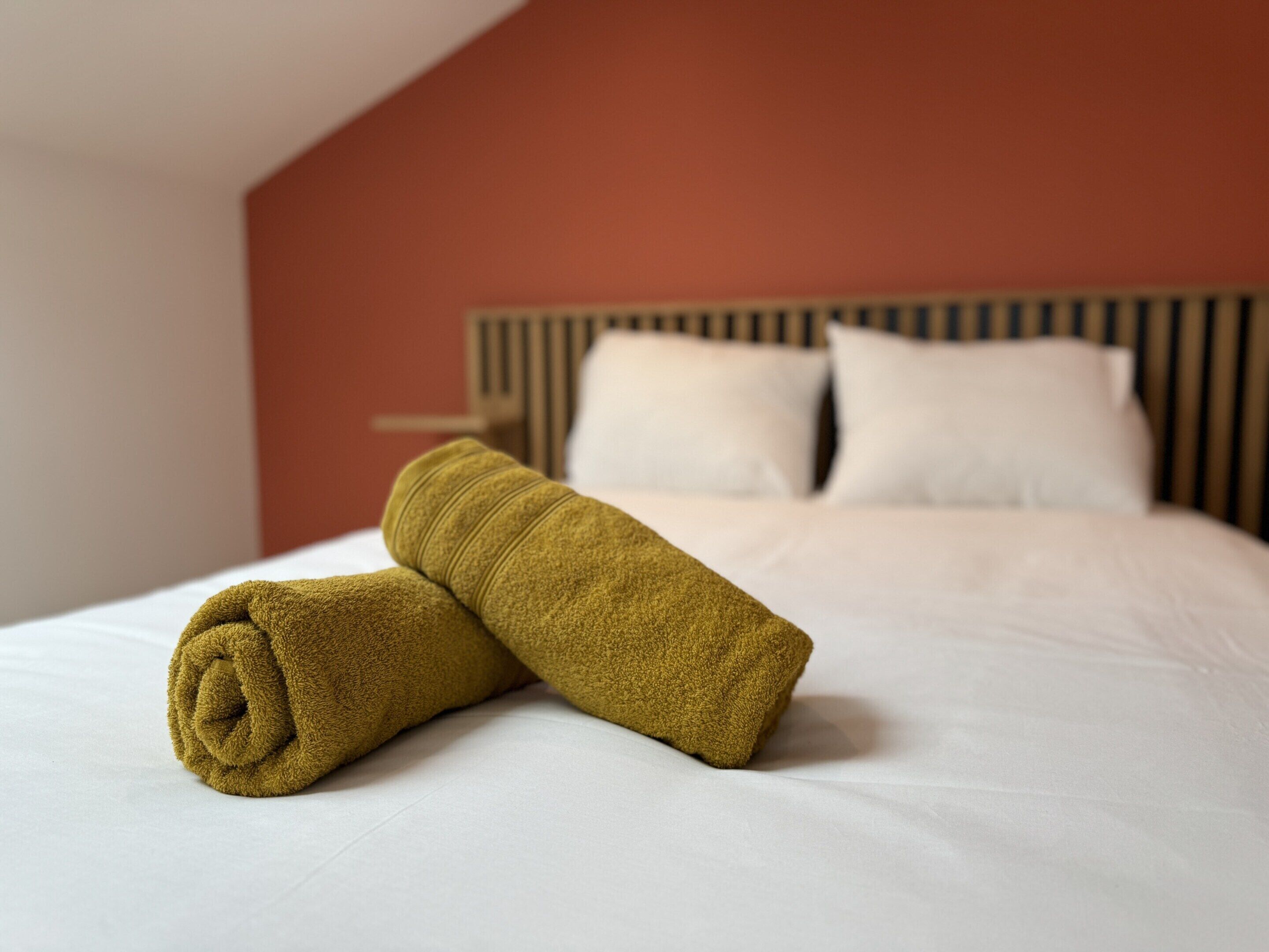 A neatly made bed with a rolled towel in the foreground and a headboard with two pillows in the background.