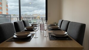 A dining table set with plates, bowls, glasses, and a bottle, with a view of buildings through large windows. - Le Corner - Ville - 8 Pers (Le Mans)