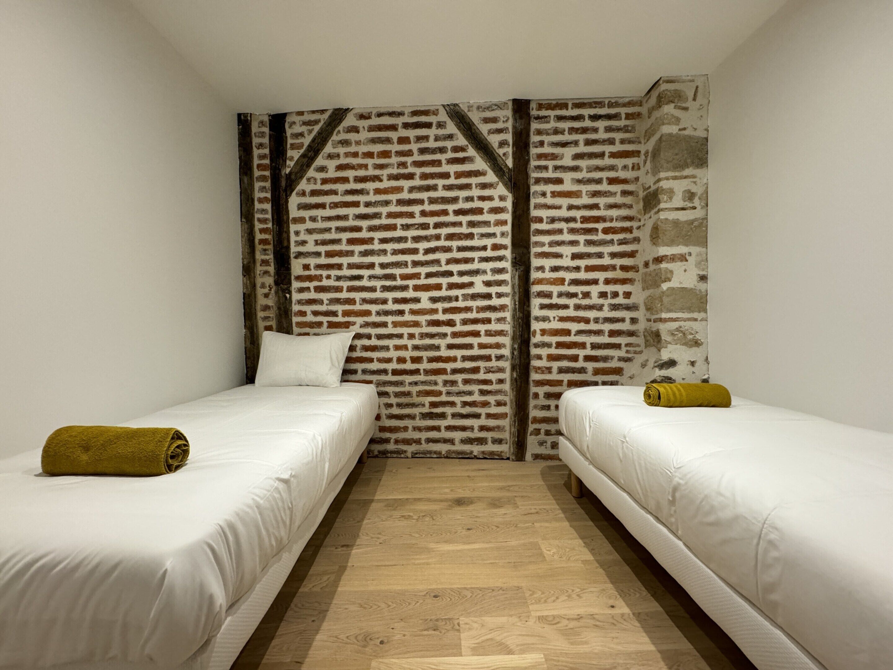 A room with two beds, a brick-patterned wall, and wooden flooring.