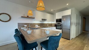 A modern kitchen with a central island, two blue chairs, pendant lights, and built-in appliances. - Le Corner - Ville - 8 Pers (Le Mans)