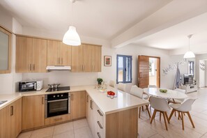 A modern kitchen with wooden cabinets, a built-in oven, and a dining area with a white table and chairs. - Protaras Seaside Villa Protamare 32 (Protaras)
