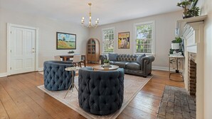 A spacious living room with a large sofa, ottoman, and a dining area. - Downtown Huntsville Gem, 2BR Walk to the Square! (Huntsville)