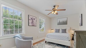 A bedroom with a bed, a chair, a ceiling fan, and large windows. - Downtown Huntsville Gem, 2BR Walk to the Square! (Huntsville)
