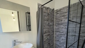 A modern bathroom with a white marble sink, a glass shower enclosure, and a stone-textured wall. - 3-bedroom Apartment With Premium Amenities (Noyen-sur-Sarthe)