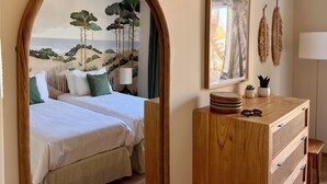 Een slaapkamer met een bed, een houten dressoir, een spiegel en een strandfries.