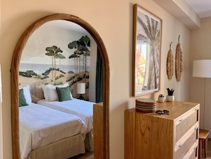 Quarto com cama, penteadeira de madeira, espelho e um mural com tema praiano.
