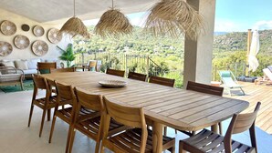 Ein Holzespeisesaal mit Stühlen, hängende Rattanlampen und Blick auf eine üppige Landschaft.