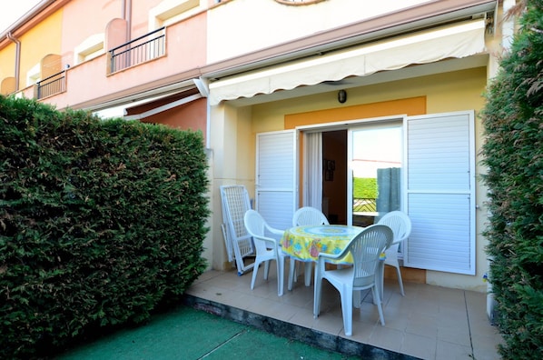 Une petite terrasse extérieure avec une table et des chaises, un auvent blanc et une haie.
