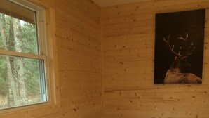 Una habitación de cabaña de madera con una cama, una ventana y un cuadro de un ciervo en la pared.