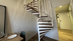 A modern interior with a spiral staircase, a dining area with a table and chairs, and a hallway leading to another room.