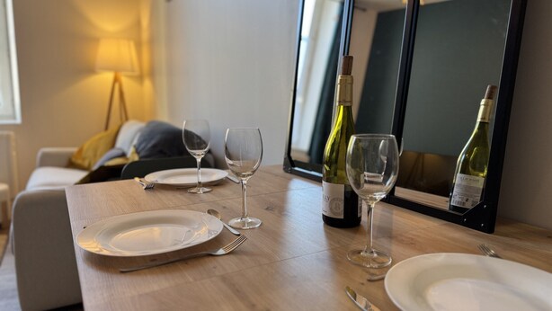A dining table with wine glasses, plates, and cutlery, a bottle of wine, and a mirror reflecting the room.