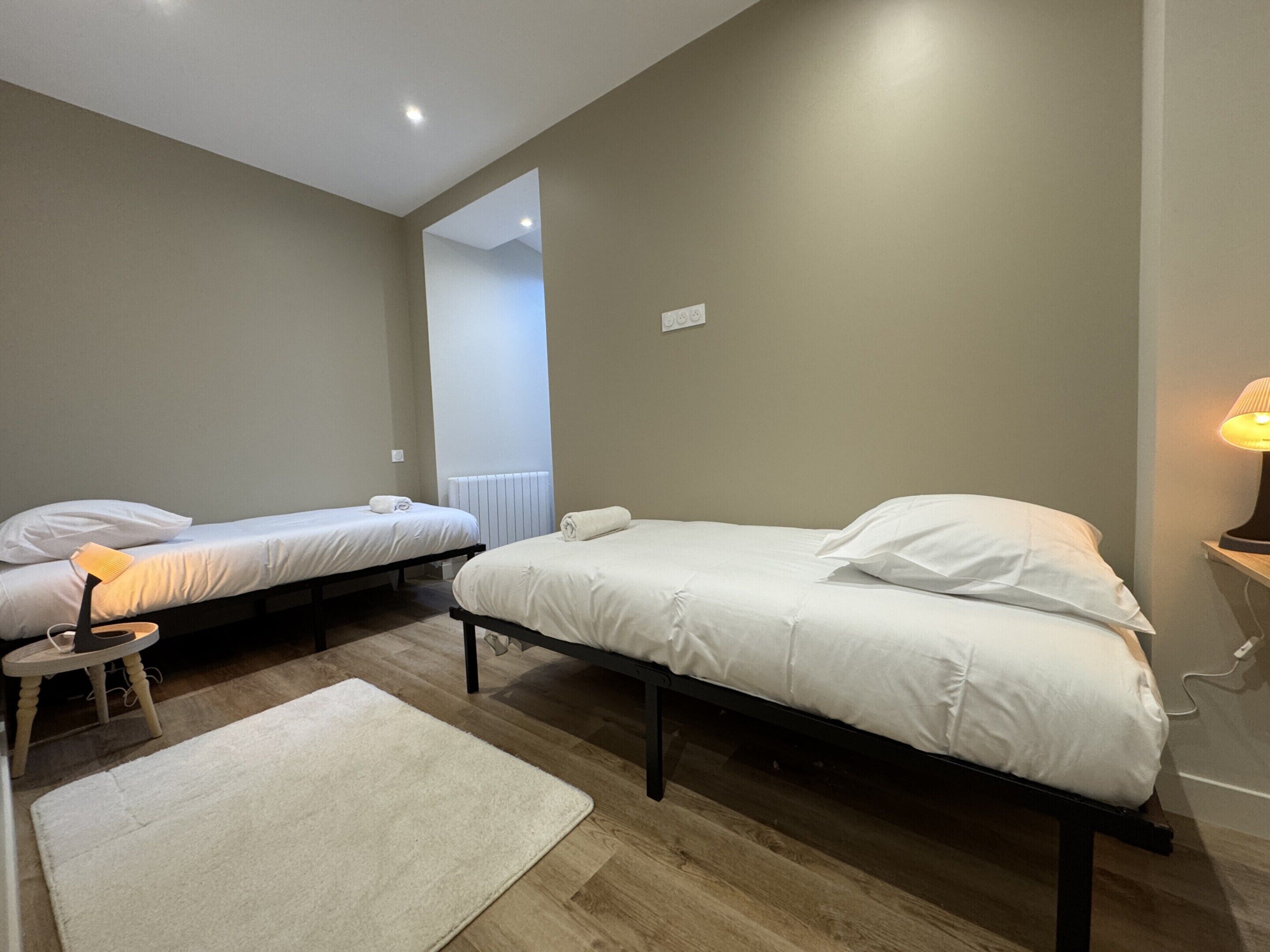 A bedroom with two single beds, a small table with a lamp, and a white rug.