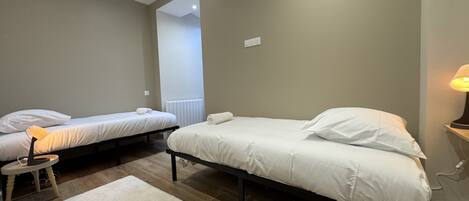 A bedroom with two single beds, a small table with a lamp, and a white rug.
