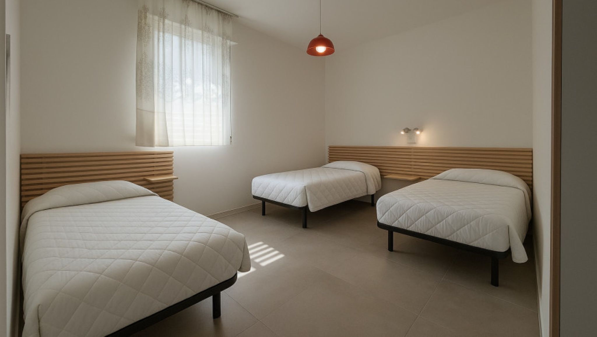 Een kamer met drie bedden, een raam met dunne gordijnen en een hanglamp.