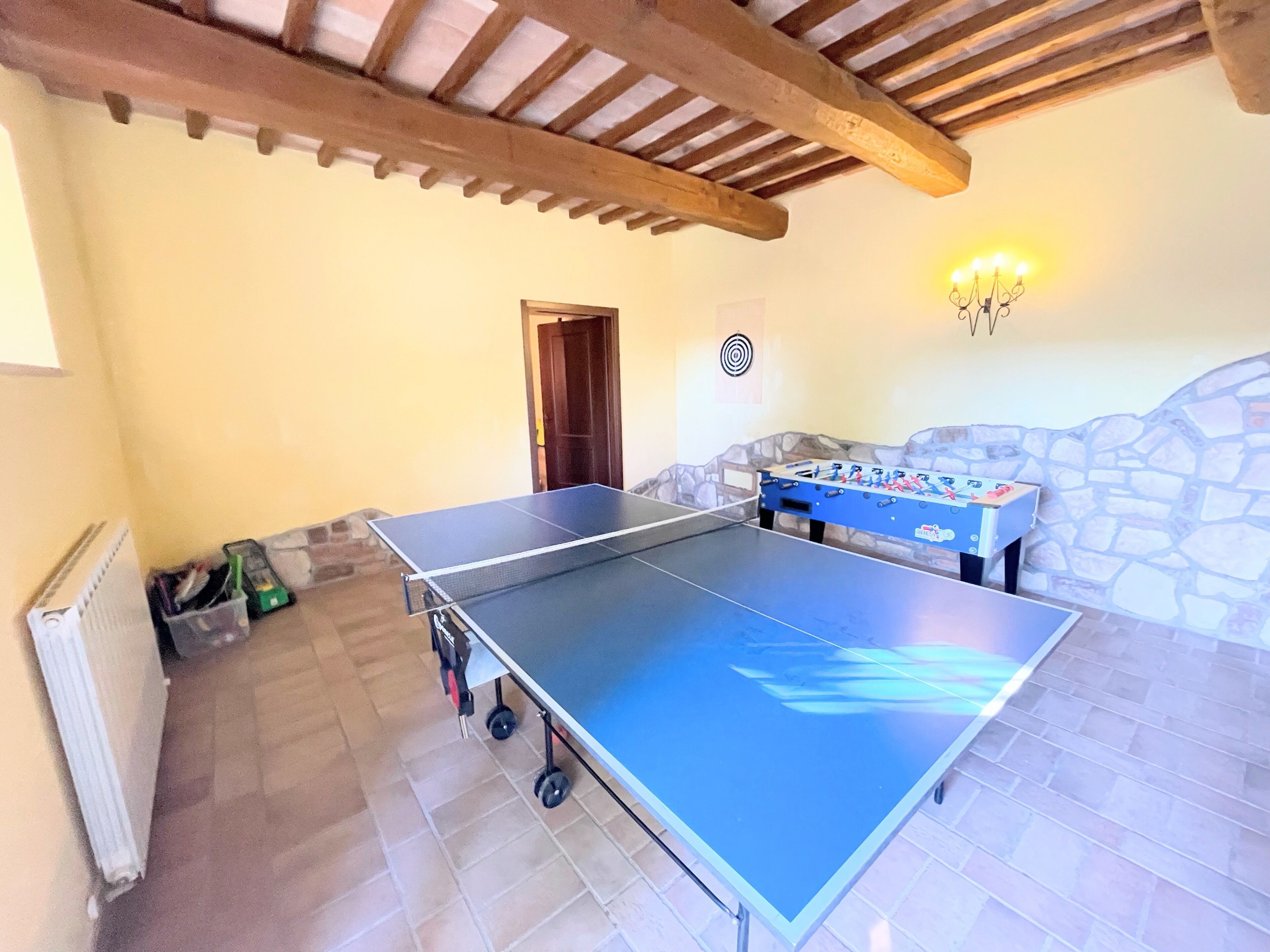 A ping pong table with a foosball table in a room with stone walls and a wooden ceiling.
