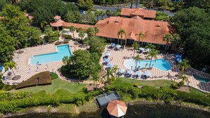An aerial view of a resort with two swimming pools, palm trees, and a checkered patio area.