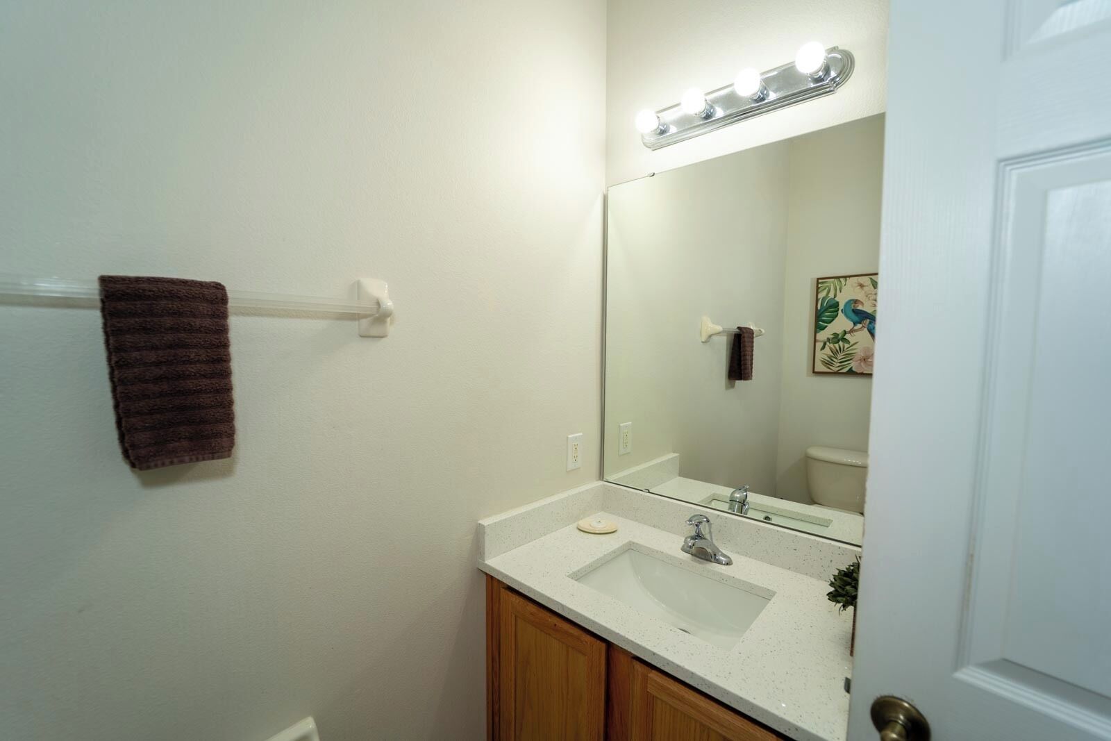 Une salle de bain avec un lavabo blanc, un miroir avec éclairage, un porte-serviettes et une porte.