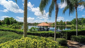A gazebo by a lake with well-maintained hedges and palm trees.