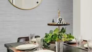 A dining area with a wooden table set for four, a round mirror on the wall, and a hanging light fixture.