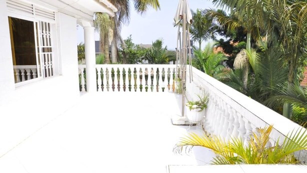 Un edificio blanco con balcón, palmeras y plantas en macetas.