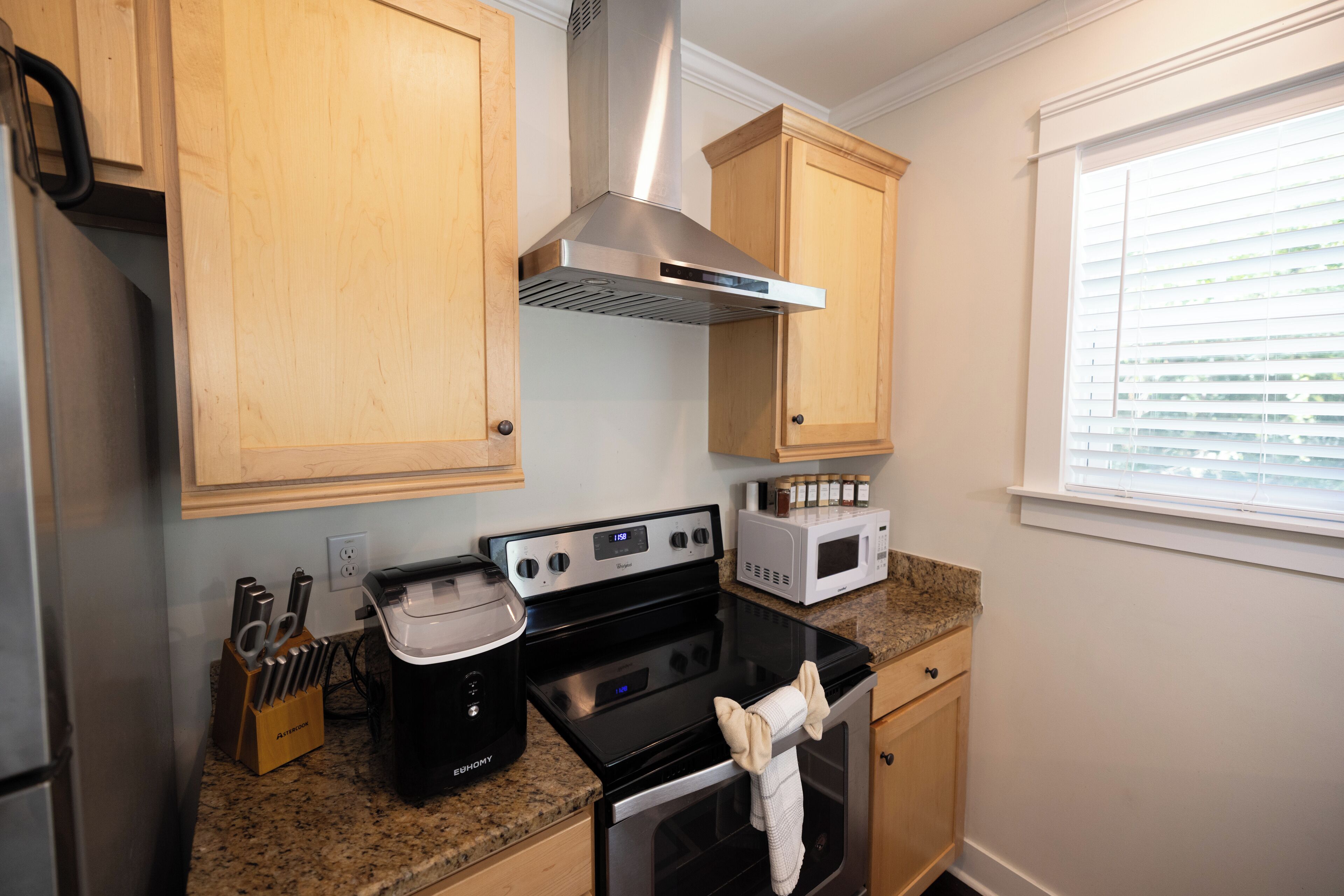 A kitchen with wooden cabinets, a stainless steel range hood, a microwave, and a stove.