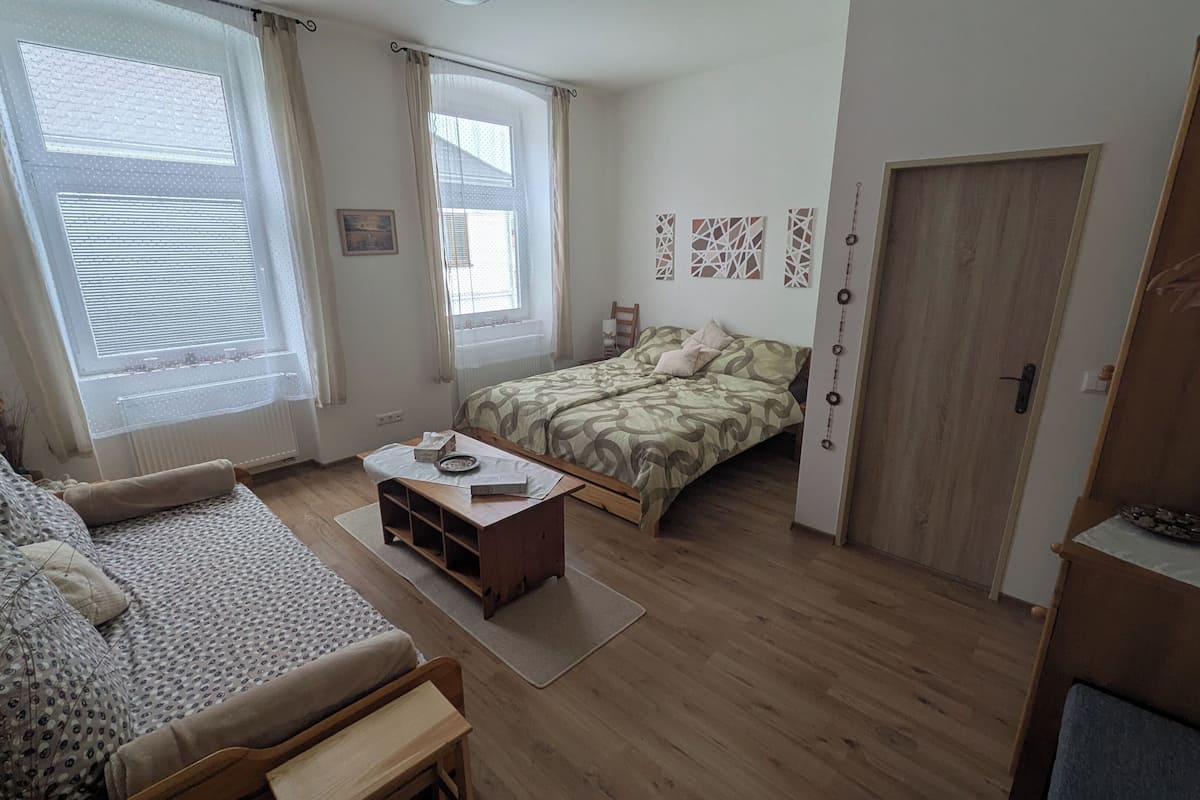 Una habitación pequeña y acogedora con cama, sofá, una mesita de madera y una puerta.