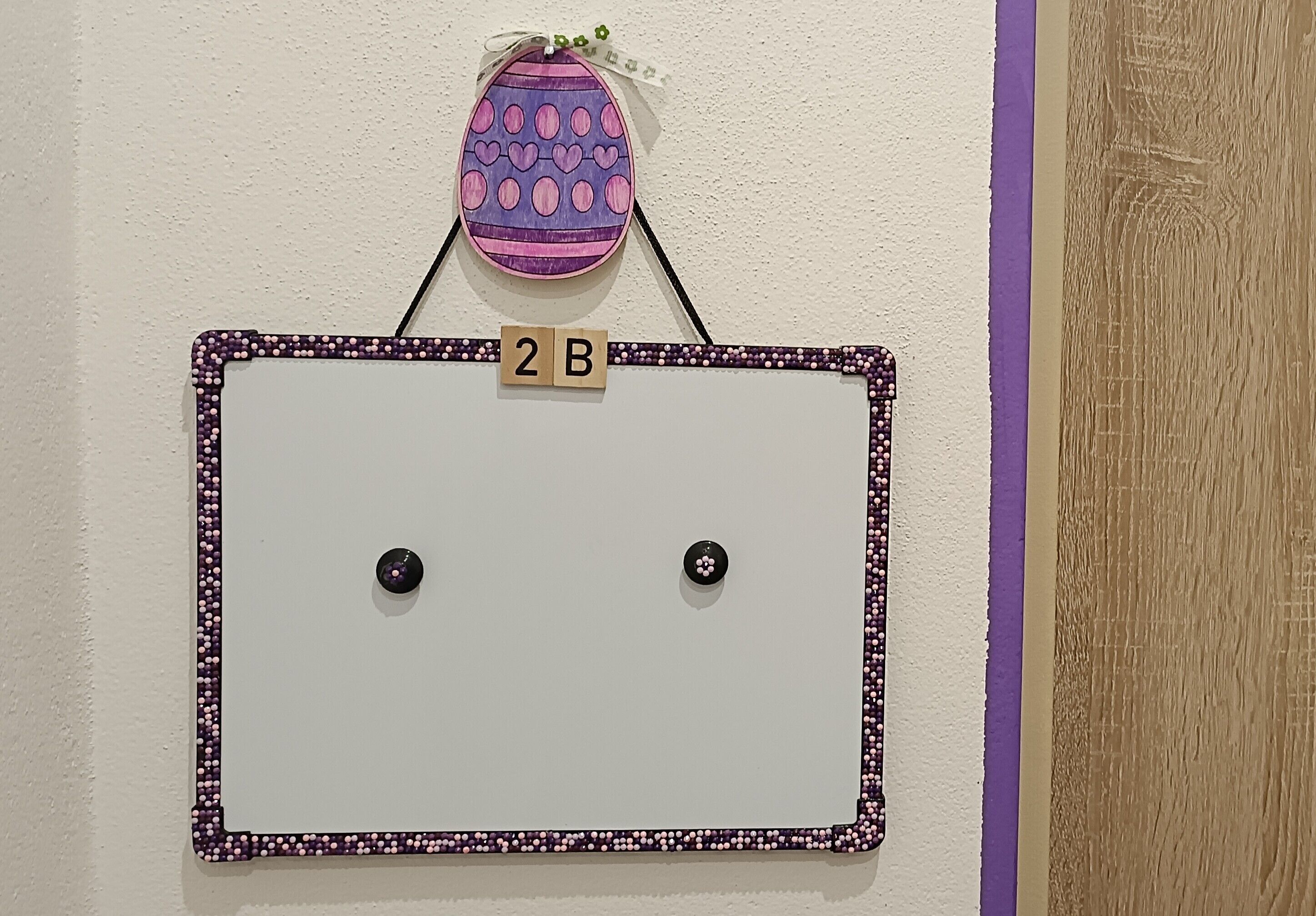 Un cuadro enmarco con borde morado y dos botones negros, colocado sobre una pared con una franja púrpura.