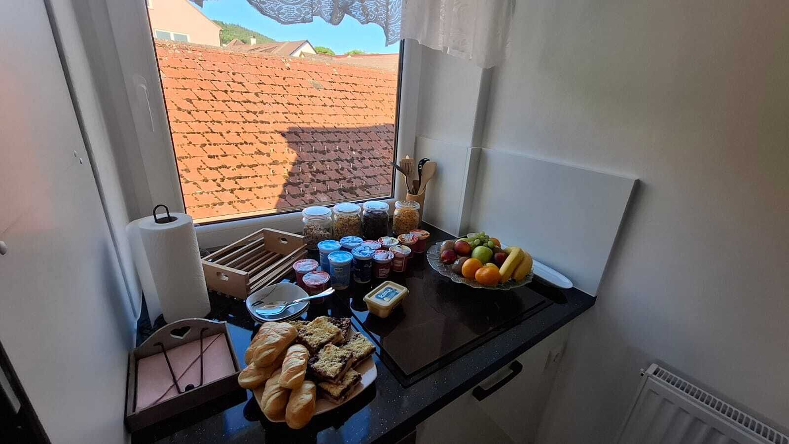 Une petite cuisine équipée avec divers produits alimentaires et une fenêtre donnant sur un toit recouvert de tuiles.