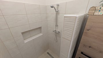 A shower area with a handheld showerhead, a built-in shelf, and a wooden cabinet.