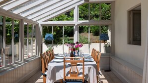 A conservatory with a table set for dining, surrounded by chairs, and a vase with flowers. - Thatchways -  a house that sleeps 7 guests  in 4 bedrooms (Thurlestone)