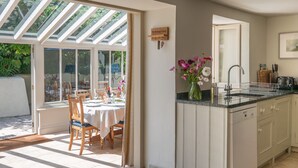 A kitchen with a built-in dishwasher, a sink, and a dining area with a table and chairs. - Thatchways -  a house that sleeps 7 guests  in 4 bedrooms (Thurlestone)