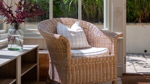 A wicker chair with a cushion in a sunlit room with large windows overlooking a garden. - Sea Lavender -  a house that sleeps 9 guests  in 5 bedrooms (Thurlestone)