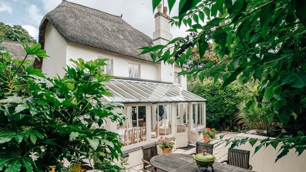 A house with a thatched roof, a conservatory, and a patio with a table and chairs. - Sea Lavender -  a house that sleeps 9 guests  in 5 bedrooms (Thurlestone)