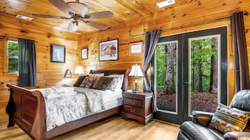 Une chambre à coucher dans un chalet en bois, avec un lit, des tables de chevet, une chaise et une grande fenêtre donnant sur la forêt.