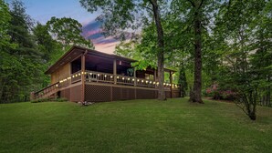 Une cabane en bois dotée d’une terrasse, entourée d’une végétation luxuriante et d’arbres.