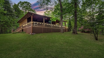 Une cabane en bois dotée d’une terrasse, entourée d’une végétation luxuriante et d’arbres.