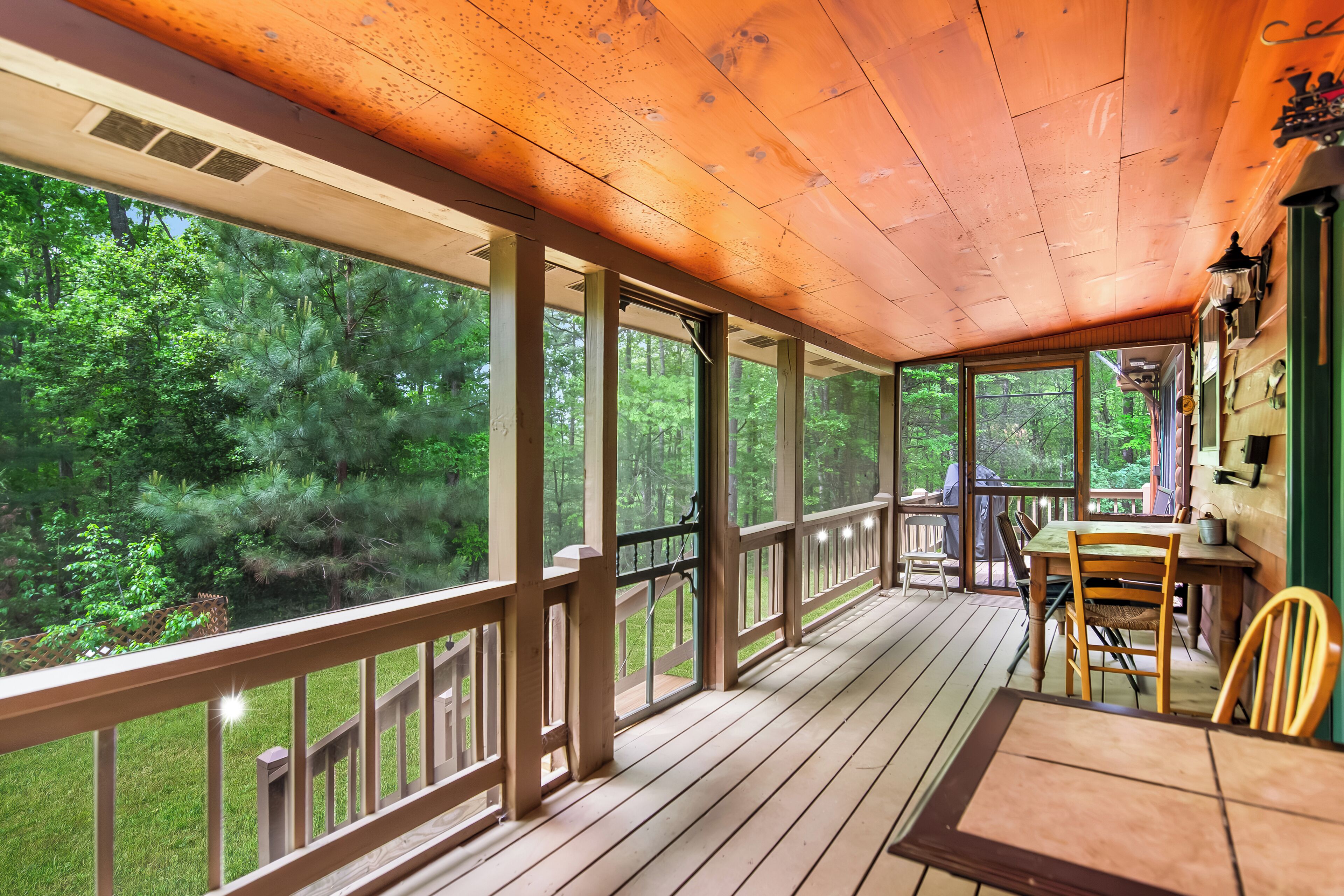 Une terrasse en bois avec une table et des chaises, de grandes fenêtres et une vue sur une forêt.