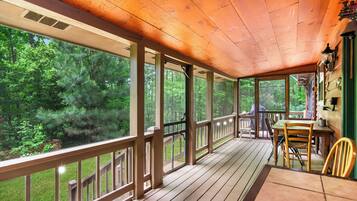 Une terrasse en bois avec une table et des chaises, de grandes fenêtres et une vue sur une forêt.