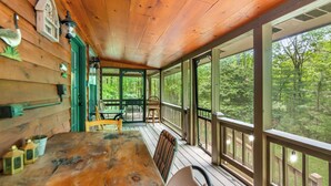 Une terrasse en bois avec une table et des chaises, de grandes fenêtres et une vue sur une forêt.