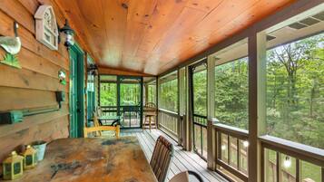 Une terrasse en bois avec une table et des chaises, de grandes fenêtres et une vue sur une forêt.