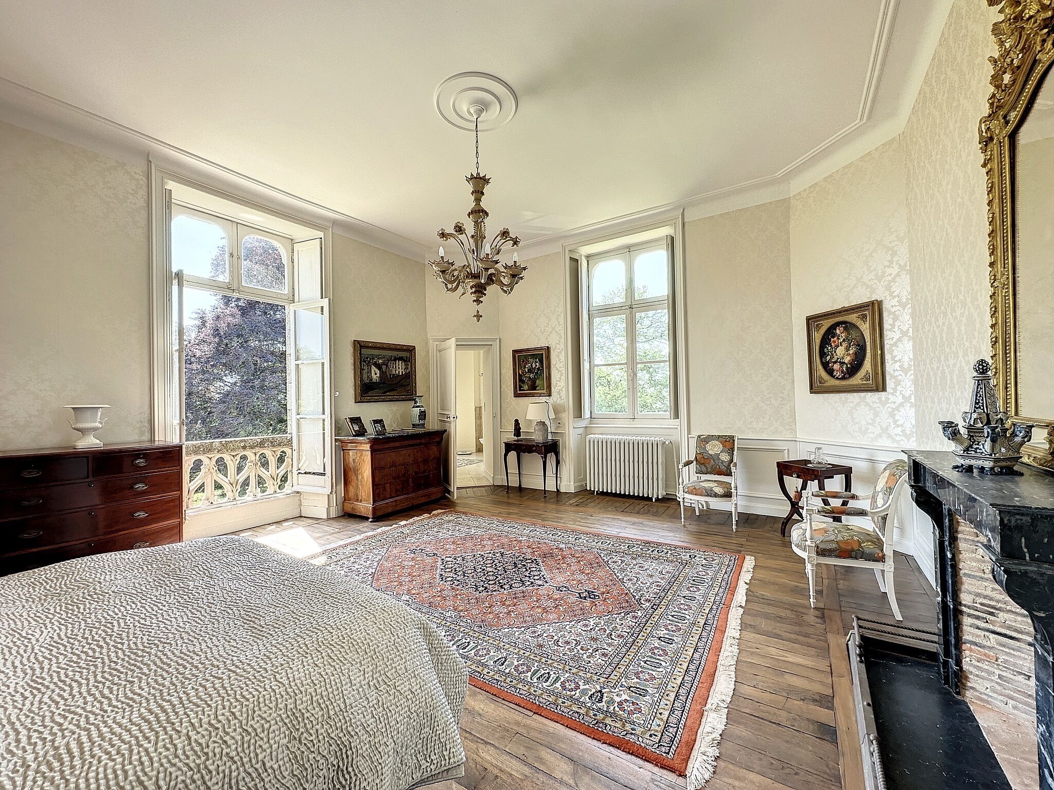 Una habitación amplia con piso de madera, un tapete estampado, chimenea y un candelabro.