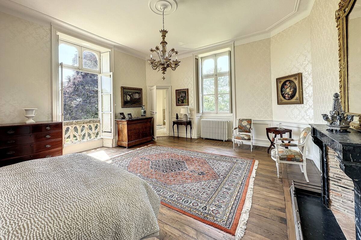 A spacious room with a large wooden floor, a patterned rug, a fireplace, and a chandelier.