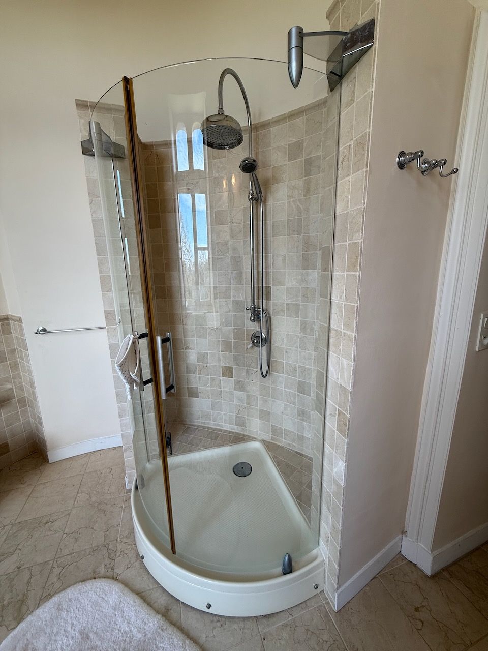 A glass-enclosed shower with a handheld showerhead and a wall-mounted faucet.