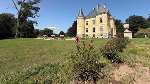 A large, yellow château with a prominent tower, surrounded by a well-maintained lawn and a few lounge chairs. - Coin de Paix - Château de Launay (Saint-Vincent-sur-Oust)