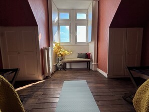 Une pièce avec un plancher en bois, un banc avec des coussins, un radiateur et une fenêtre donnant sur le ciel.