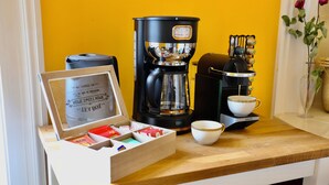 Eine Kaffeemaschine, eine Tasse und eine Packung Kaffeekapseln auf einer Holztischplatte.